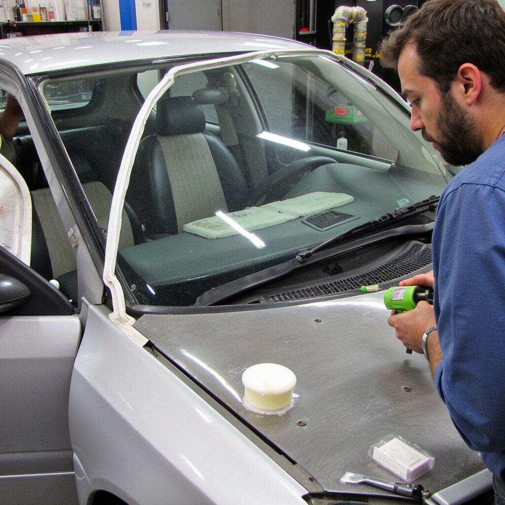 Technician applying windscreen bonding glue to a car window with precision in a professional workshop.